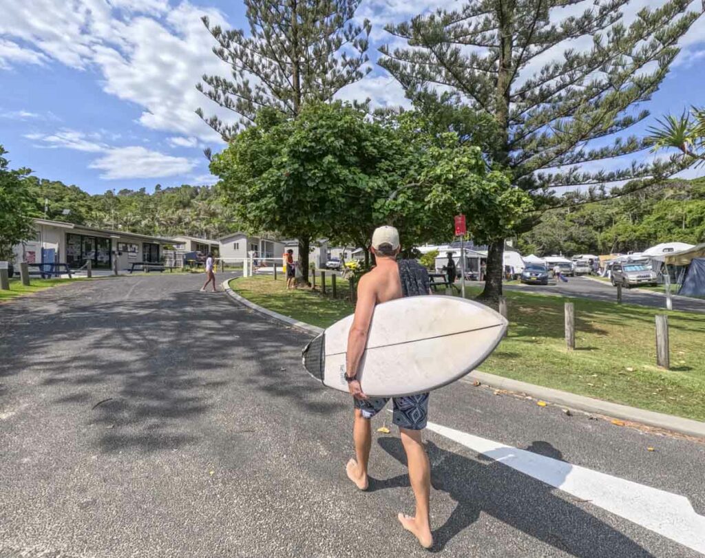 A man holding a surfboard and walking to the entrance of Broken Head Holiday Park