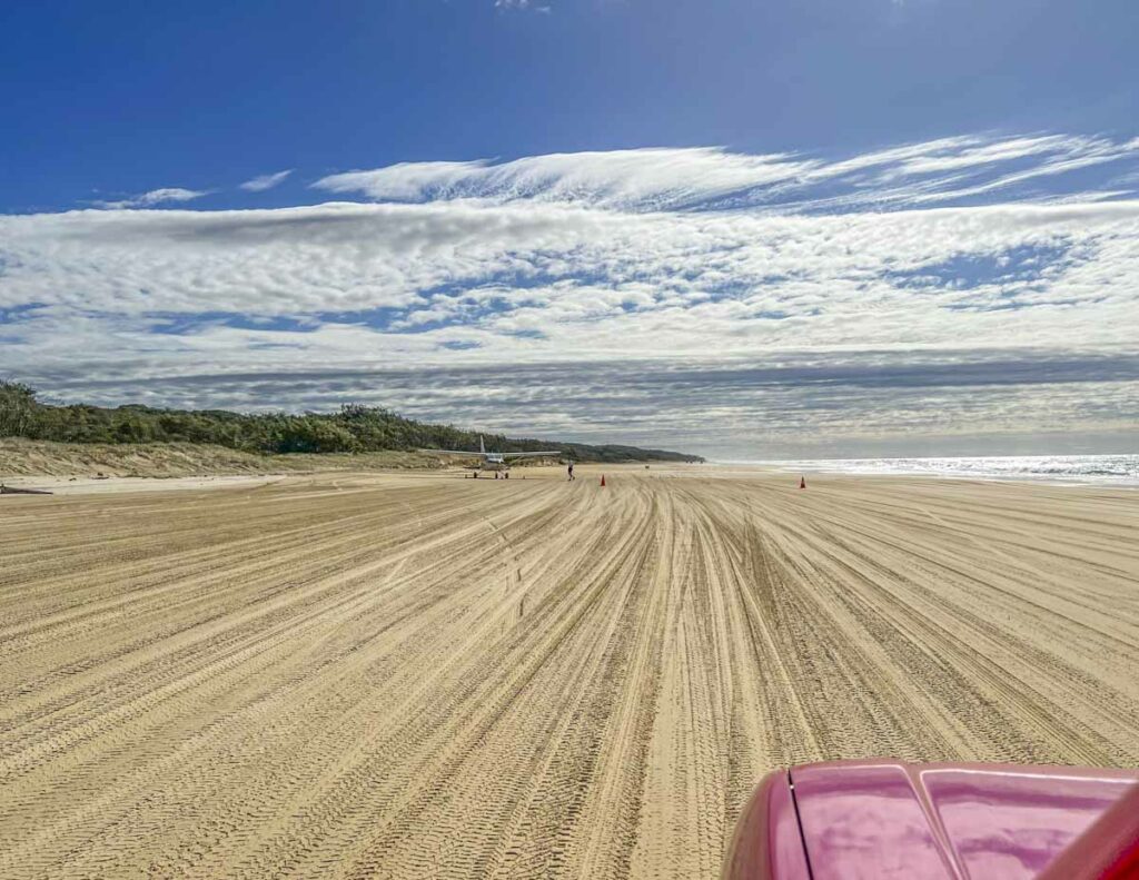 A car driving on a long stretch of beach on Fraser Island